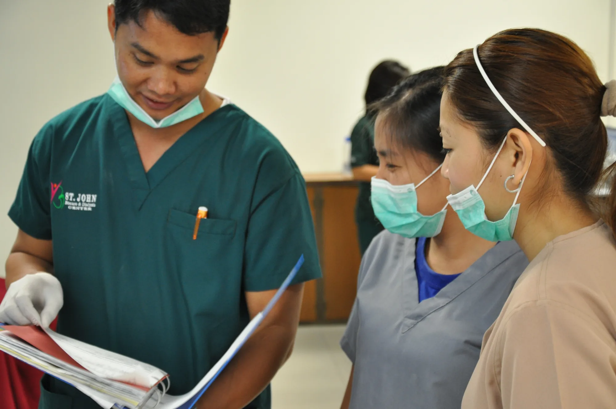 A St. John Biocare senior nurse reviewing a patient chart with two trainee nurses